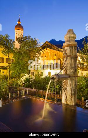 Fountain and illuminated church in Garmisch-Partenkirchen, Bavaria, Germany Stock Photo