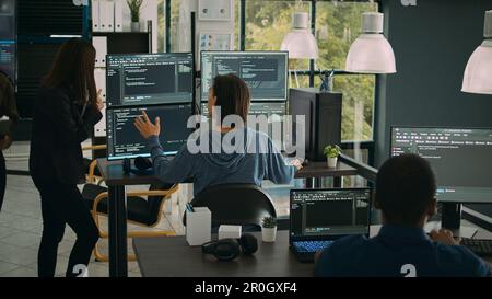 System engineer checking code on multiple monitors and working with app developer colleague in it agency office. Coder analyzing algorithm on screens, developing new user interface. Stock Photo