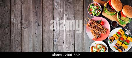 Summer BBQ or picnic food side border. Selection of burgers, grilled meat, vegetables, fruits, salad and potatoes. Overhead view on a dark wood banner Stock Photo