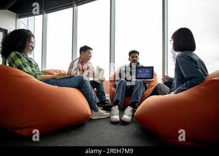 Diverse team of adults in casual clothes leveraging modern devices while working in creative office. Car designers developing digital vehicle model using computer-aided programs in meeting space. Stock Photo