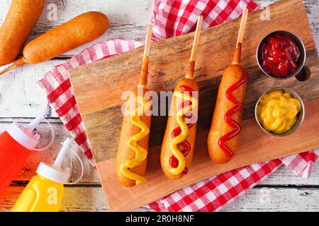 Corn dogs with mustard and ketchup. Top view table scene over a white wood background. Stock Photo