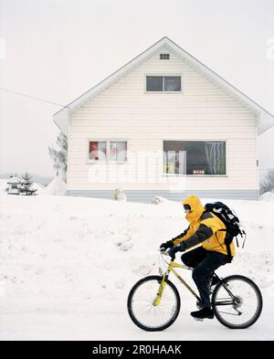 CANADA, man riding bicycle in snow in front of house, Fernie Stock Photo