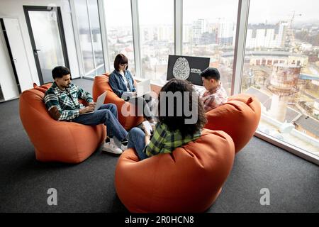 Full length view of diverse professionals working on gadgets while staying in open office with AI presentation on display. Efficient scientists developing online customer support system in office. Stock Photo