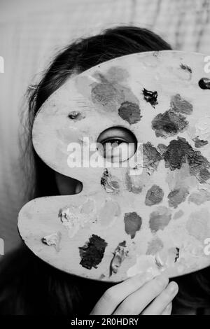 This black and white photo capture an artist peering into a hole in her paint palette where oil paints have been mixed. A new perspective on the creat Stock Photo