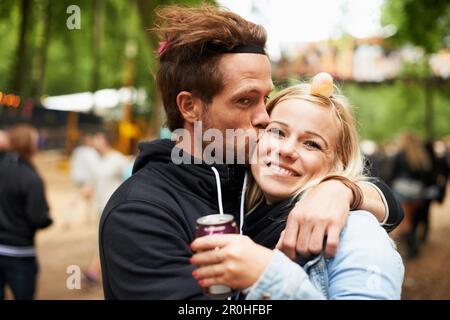 Loving in the outdoors. Portrait of a young man kissing his girlfriend while outside at a music festival. Stock Photo