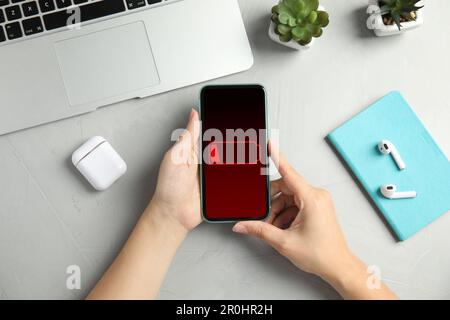 Young woman holding smartphone with low battery at grey table, top view Stock Photo