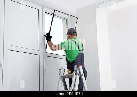 Worker on folding ladder installing window indoors Stock Photo