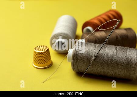 Different colorful sewing threads with needle and thimble on yellow background, closeup Stock Photo