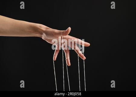 Woman pulling strings of puppet on black background, closeup Stock Photo