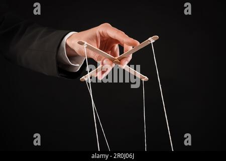 Woman pulling strings of puppet on black background, closeup Stock Photo