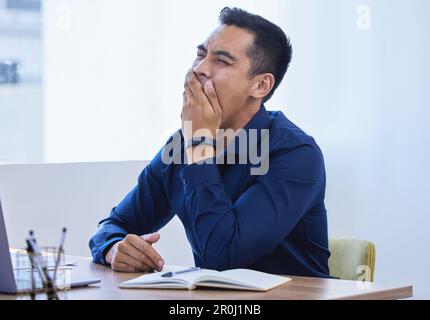 I just want t go home to my bed...a young businessman yawning while working in an office. Stock Photo