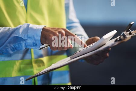 Adding up for the final stock count. an unrecognizable contractor standing alone in the warehouse and using a calculator during stock-take. Stock Photo