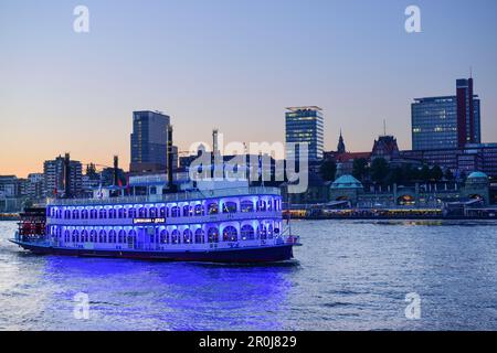 Illuminated paddle wheel ship Louisiana Star sailing on the river Elbe, St. Pauli-Landungsbruecken in the background, Hamburg, Germany Stock Photo