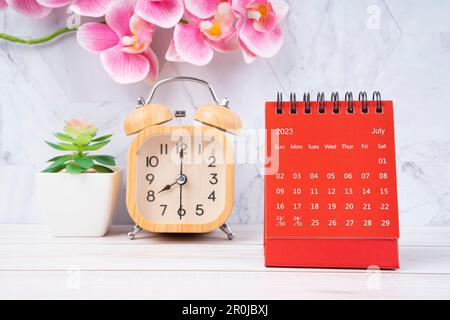 Red calendar July 2023. Desk calendar for year 2023 and pink orchid on wooden background. Stock Photo