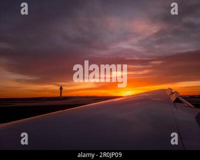 Gorgeous sunset view with orange, pink, purple sky as the plane lands at Washington Dulles and passes the control tower Stock Photo