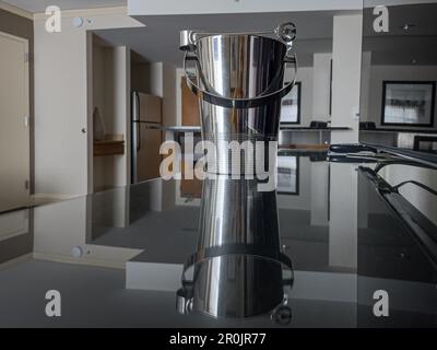 Stainless steel ice bucket reflecting off a mirror glass table in a hotel room Stock Photo