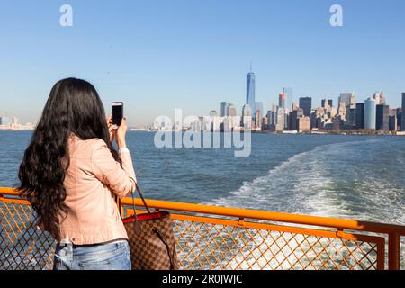 Asian woman with taking pictures with her cellphone, mobile phone, Ferry to Staten Island, view over the Hudson to downtown Manhattan and the new  One Stock Photo