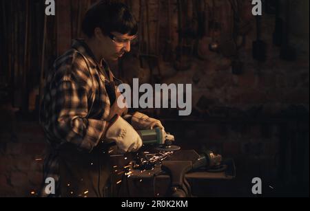 She does amazing things with metal. a young woman using an angle grinder while working at a foundry. Stock Photo