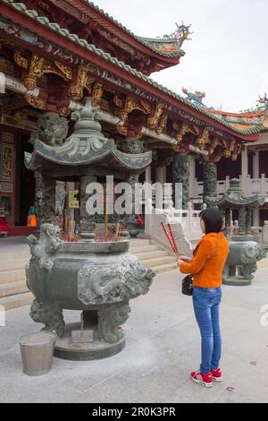 Praying woman holds incense during worship ceremony at A-Ma Cultural Village, Coloane, Macau, China Stock Photo