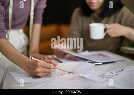 Close-up image of two professional female fashion designers or dressmakers sketching their new design and working in the studio together. Stock Photo