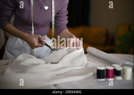 Close-up image of a dressmaker or fashion designer using scissors to cut the fabric, making fabric pattern, working in her studio. Stock Photo