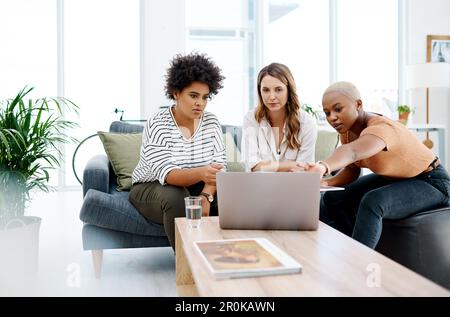 Their company thrives through dedicated teamwork. a group of businesswomen working together on a laptop in an office. Stock Photo