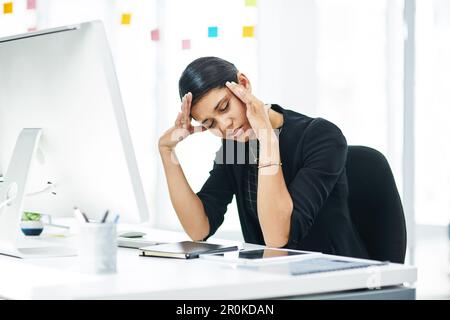 Coping with stress at work is easier when you understand the triggers. a young businesswoman looking stressed out while working in an office. Stock Photo