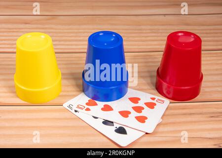 Hat game with play cards and red, blue and yellow dice cups on wooden floor Stock Photo