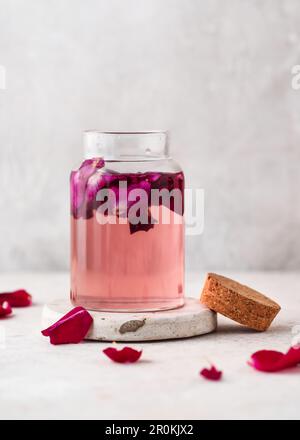 Homemade rose water in a glass bottle with pink petals in it. Concept of beauty and care. Selective focus. Copy space. Stock Photo