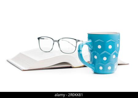 The polka dot mug with book and glasses isolated on the white background. Stock Photo