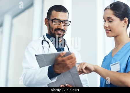 Lets put all of the symptoms together. two young doctors using a digital tablet in a modern hospital. Stock Photo