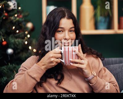 Curling up on the couch with some Christmas cocoa. a beautiful young woman enjoying a warm beverage on the sofa during Christmas at home. Stock Photo