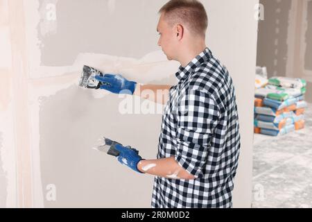 Man plastering wall with putty knife indoors. Home renovation Stock Photo