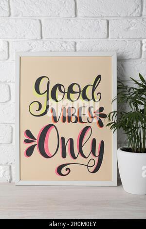 Board with phrase Good Vibes Only and houseplant on wooden table near white brick wall Stock Photo