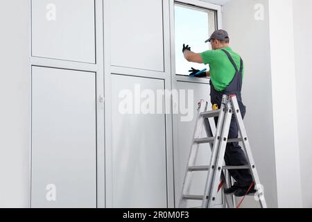 Worker on folding ladder installing window indoors Stock Photo