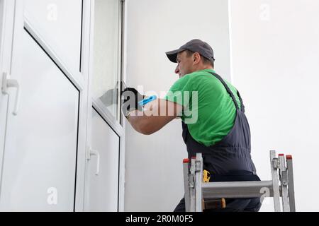 Worker on folding ladder installing window indoors Stock Photo