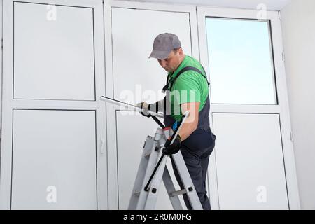 Worker on folding ladder installing window indoors Stock Photo