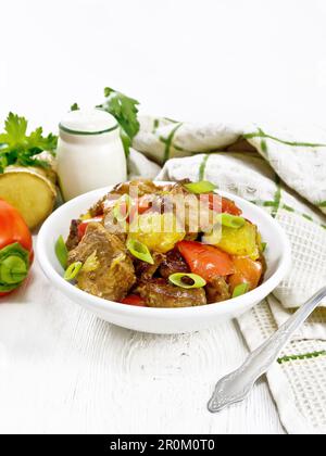 Beef with oranges, bell pepper and ginger root in bowl, a towel and a fork on white wooden board background Stock Photo