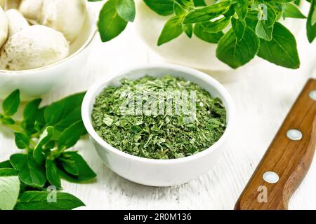 Dried oregano in bowl, oregano branches with leaves in a mortar, champignons and a knife on white wooden board background Stock Photo