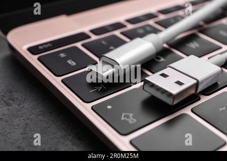 USB cable with type C connector and laptop on dark table, closeup Stock Photo
