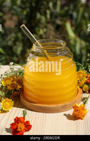 Taking delicious fresh honey with dipper from glass jar surrounded by beautiful flowers on table in garden Stock Photo