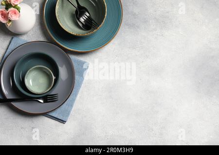 Stylish tableware and vase with beautiful roses on light grey table, flat lay. Space for text Stock Photo
