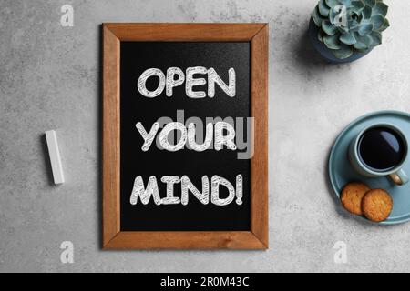 Small chalkboard with motivational quote Open your mind, coffee and cookies on light grey table, flat lay Stock Photo