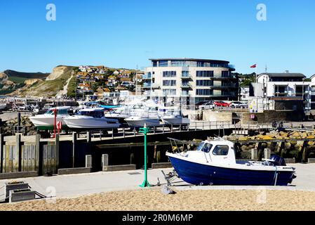 Boats in dry dock with the Ellipse building and along the quayside to the rear, West Bay, Dorset, UK, Europe. Stock Photo