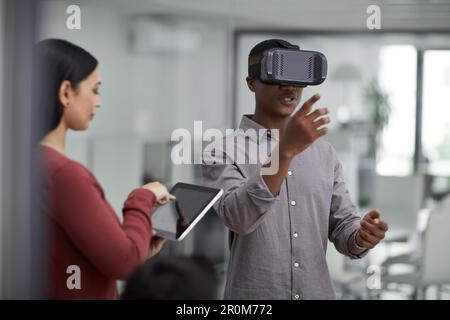 Developing a brand new virtual reality app. two young colleagues using a digital tablet and a virtual reality headset in a modern office. Stock Photo