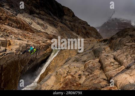 A female hiker crosses the Rio Electrico on a zip line (Tirolesa), rocks in the foreground, Los Glaciares National Park, Patagonia, Argentina Stock Photo