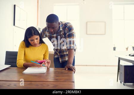 Mobile app developers hard at work. a young businessman and businesswoman using a mobile phone together in a modern office. Stock Photo