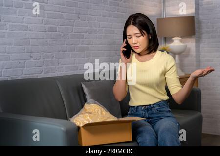 Young Asian woman complaining on mobile phone when she received a wrong or damaged parcel from ordering online. E-Commerce and online shopping mistake Stock Photo