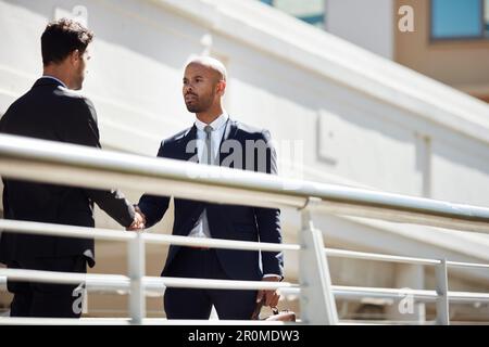 Bridging the gap between our businesses. young handsome businessmen shaking hands on a bridge outside. Stock Photo