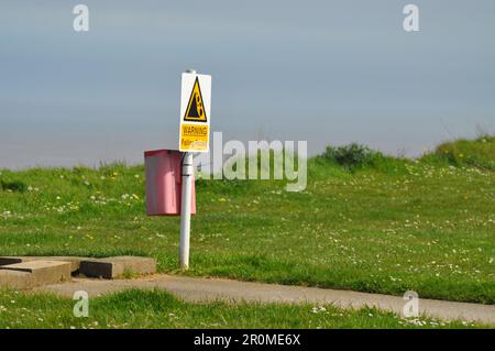 Warning sign advising of unstable cliff edge and falling rocks due to coastal erosion on cliffs at Aldbrough, East Yorkshire, England Stock Photo